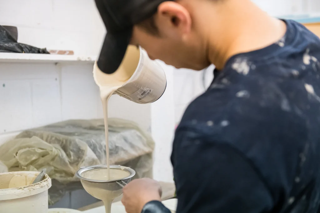 Male student in ceramics workroom pouring liquid clay