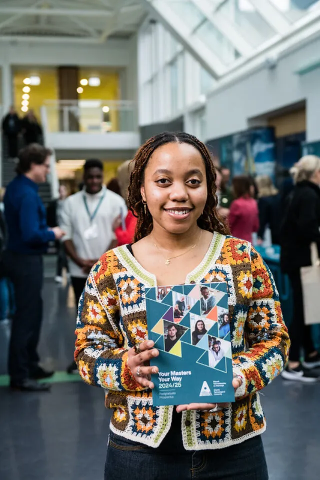 Female student in crochet top holds up 2024 - 2025 ATU Postgraduate Prospectus at Information Event