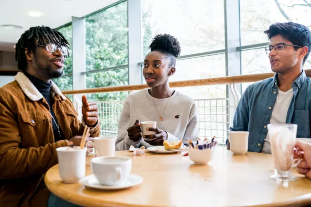 Three students sitting around table chatting and drinking coffee