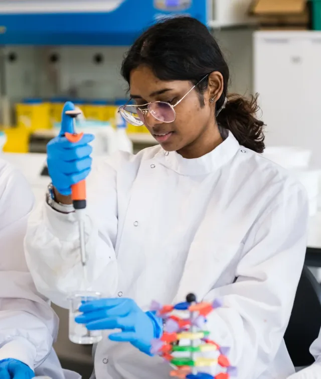 Female international student in lab coat uses a pipette in the laboratory surrounded by lab equipment