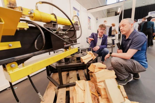 Two people look on at a saw cutting wood at the Engineering Expo.