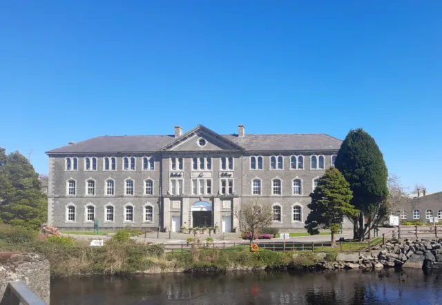 Three story building with greenery outside, situated beside a calm river.