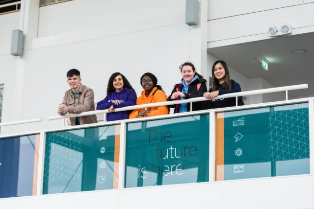 Students smiling and looking down from a balcony.