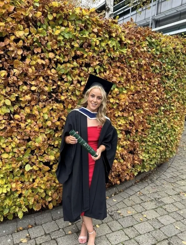 Female graduate posing with degree in graduation gown