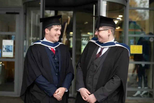 2 graduates wearing cap and gown are laughing together on their graduation day