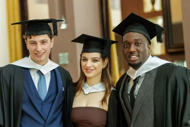 3 graduates wearing a cap and gown at graduation ceremony