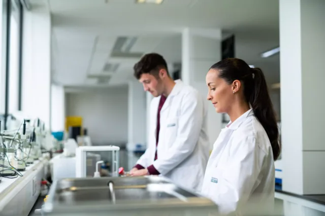 2 pharmacy students in lab coats are working beside each other
