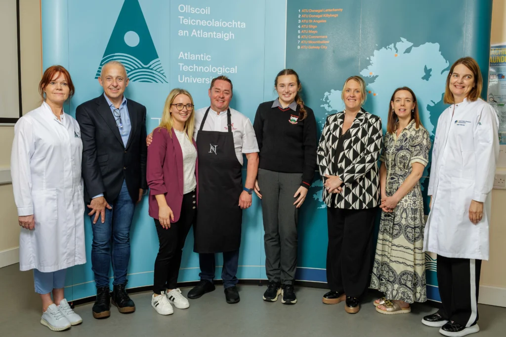 Chef Neven Maguire stands with student and teacher. Also in the photo is ATU staff and stakeholders, posed in front of a blue ATU branded backdrop featuring the university's logo and map of Ireland.