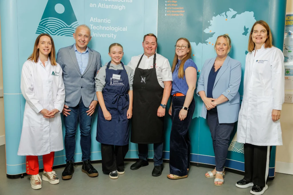 Chef Neven Maguire stands with student and teacher. Also in the photo is ATU staff and stakeholders, posed in front of a blue ATU branded backdrop featuring the university's logo and map of Ireland.