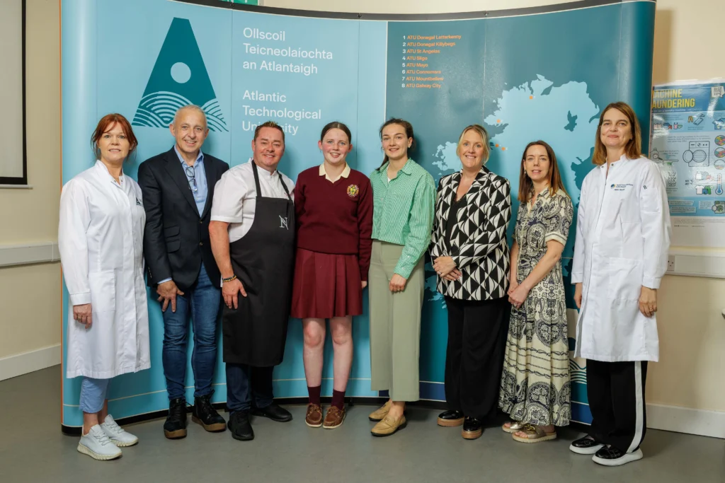 Chef Neven Maguire stands with student and teacher. Also in the photo is ATU staff and stakeholders, posed in front of a blue ATU branded backdrop featuring the university's logo and map of Ireland.