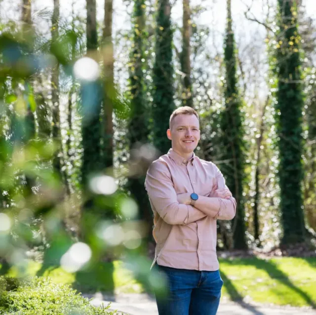 Male student standing outside with trees behind him
