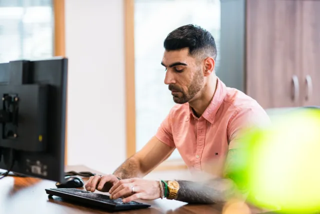 Male sitting at a computer screen typing on a keyboard