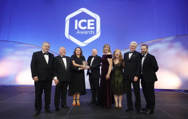 Group of people dressed in black tie on a stage accepting an award. The ICE Awards logo is the backdrop.