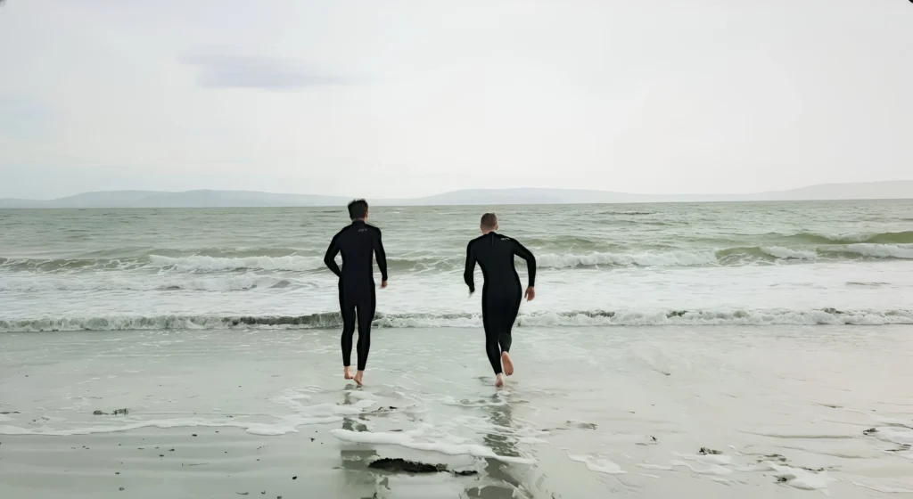 Two men in wetsuits running into the sea