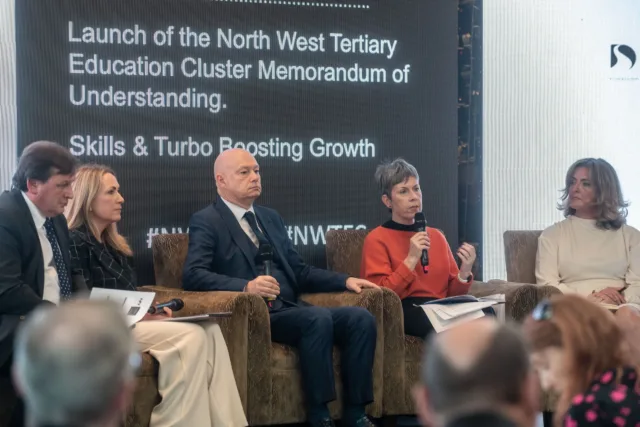 Panel of speakers sitting in armchairs facing an audience.