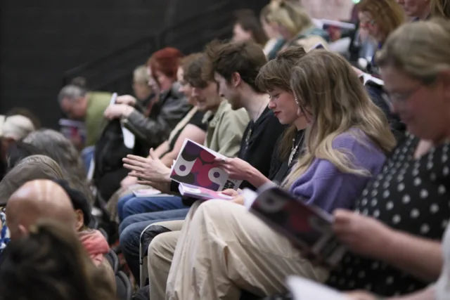 Audience members engaged in reading the newly launched Scrimshaw Journal of New Writing and Visual Art Volume 4, with open books in hand, at the event
