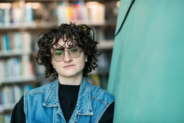 Woman with curly hair and glasses wearing denim waistcoat and black top