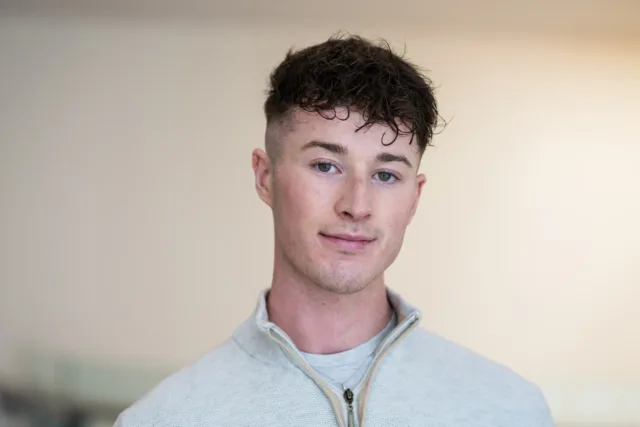 Man with black hair wearing grey jumper with zip