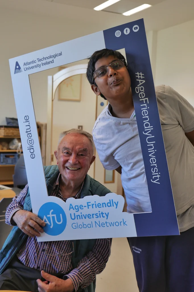 Man and student hold up a selfie frame and smile towards the camera.