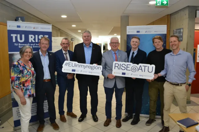Group of ATU staff and stakeholders smile holding two signs that read #EUinmyregion and RISE@ATU.
