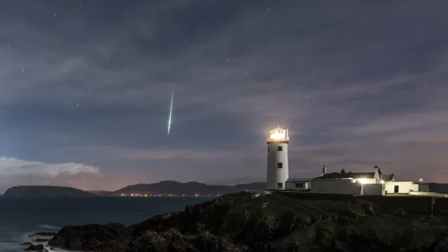 Fanad Lighthouse lit up with a starry sky and a shooting star in the background.