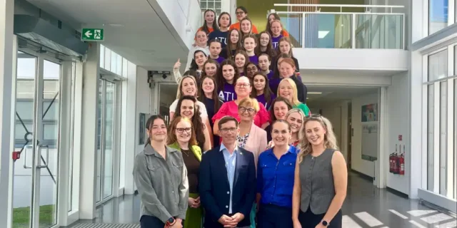 Group of students and staff stand on a staircase smiling