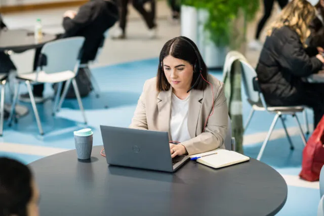 Female student, learning online at a laptop in cafe with headphones on