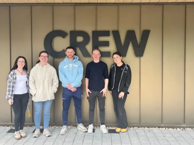 Five ATU students stand for a photo in front of the CREW building. CREW is written in back letters on the building.
