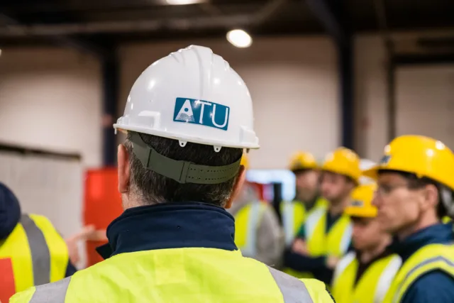 Back of someone's head wearing a hard hat with the ATU logo. The person is also wearing a high vis.