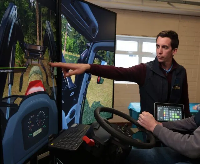 Man pointing to a digital screen displaying farming simulator in a tractor