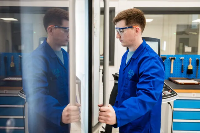 Man opening a door to a machine in a lab wearing protective goggles and a labcoat