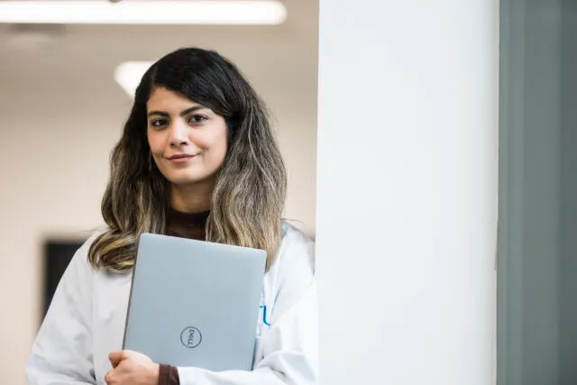 Female student in lab coat holding laptop against her chest