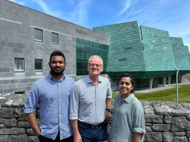 (L-R) Chethaka Gamage (Winner), Dr Ciarán Ó hAnnracháin (Chair Operational Board for the WTUN), and Dhanushi Rodrigo (Winner) pictured together at ATU Galway City, Dublin Road campus. The stand in front of the iconic green sail shaped building.
