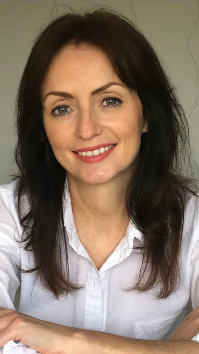 Women with arms folded smiling at camera wearing white shirt with dark straight hair.