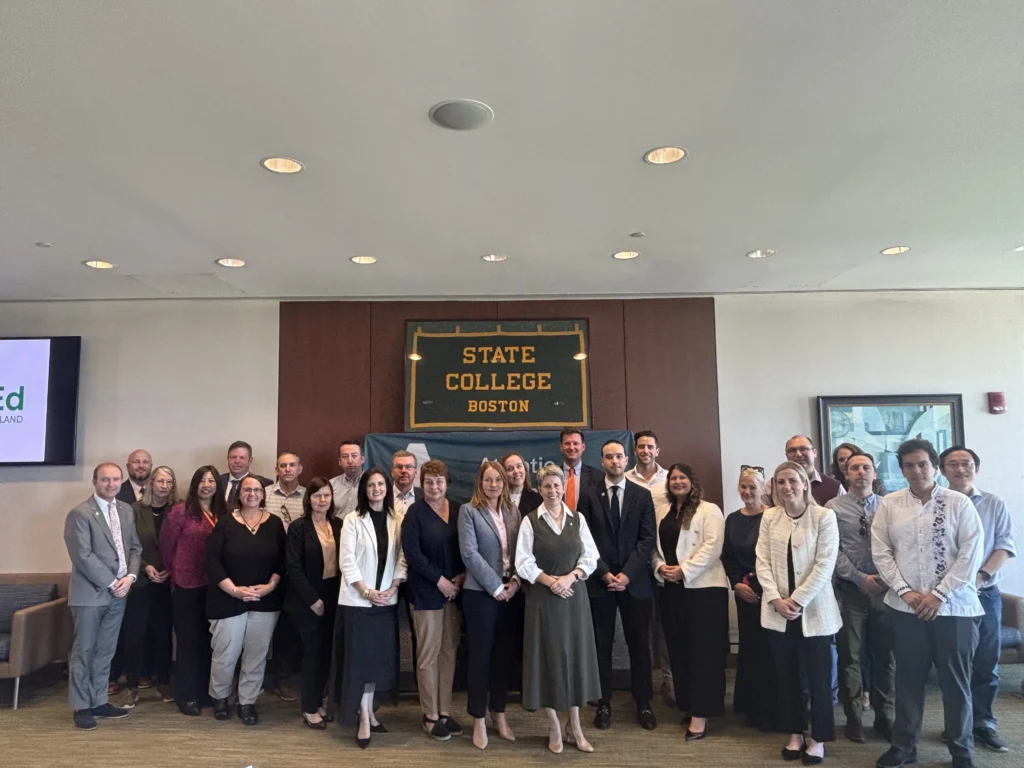 President Dr Orla Flynn pictured with a group of stakeholders, a sign that reads State College Boston is behind the group.