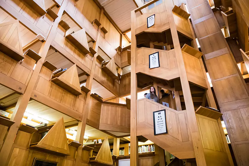 Interior of a library with a multi-level wooden architectural design, featuring staircases, platforms, and geometric shapes like triangles and rectangles.