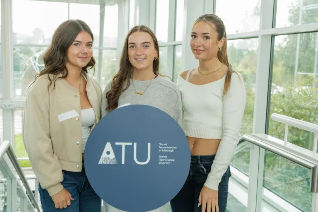 Three students holding a circular blue ATU sign