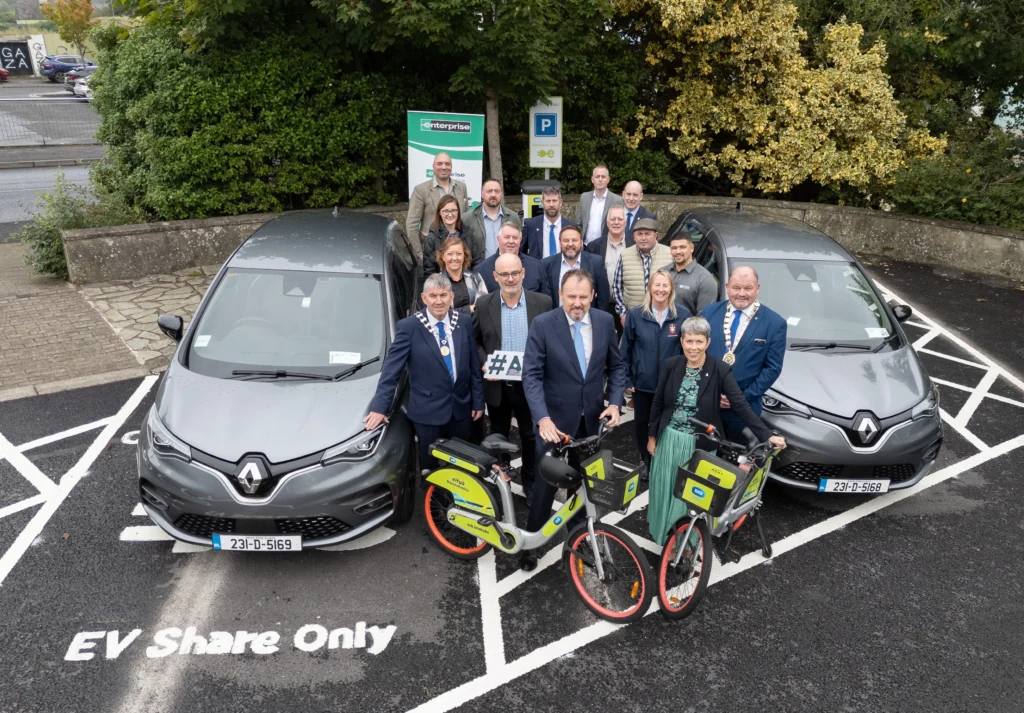 At the launch of the ROBUST eMobility Hub in Letterkenny, local leaders and stakeholders gather between two grey Renault electric cars and e-bikes