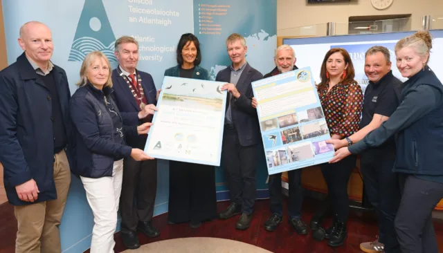 Group of ATU staff and stakeholders holding two posters.