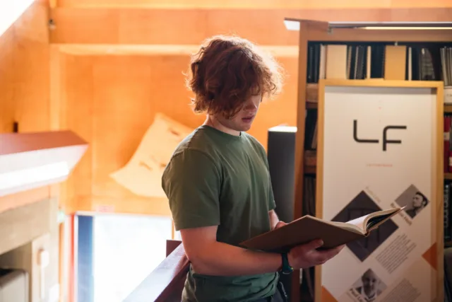 Red hair student wearing green tee shirt reads book in Library