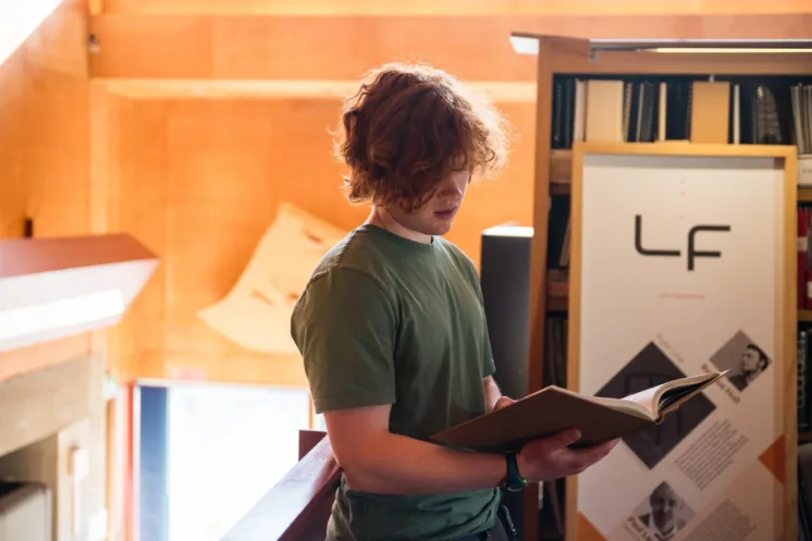 Red hair student wearing green tee shirt reads book in Library