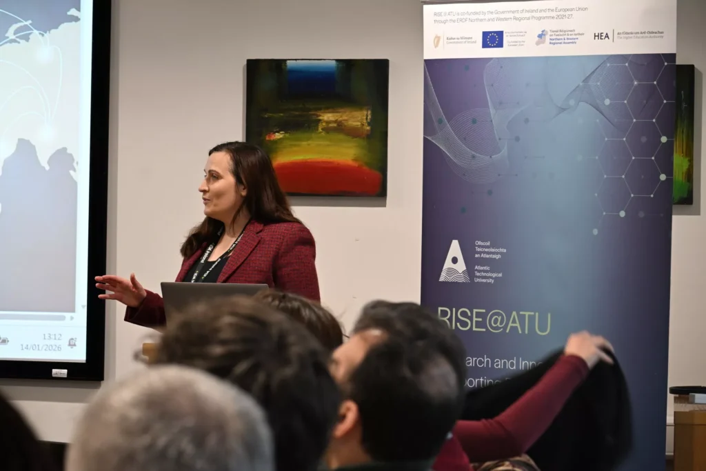 A person standing at the front of a room giving a presentation beside a large screen