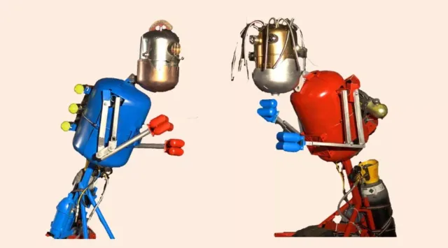 “Two colorful, retro‑styled robots face each other in boxing stances. The robot on the left is blue with red gloves, and the robot on the right is red with blue gloves.