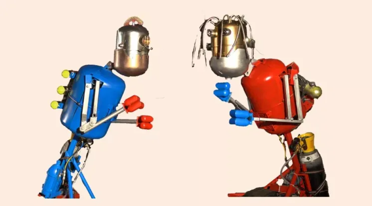 “Two colorful, retro‑styled robots face each other in boxing stances. The robot on the left is blue with red gloves, and the robot on the right is red with blue gloves.