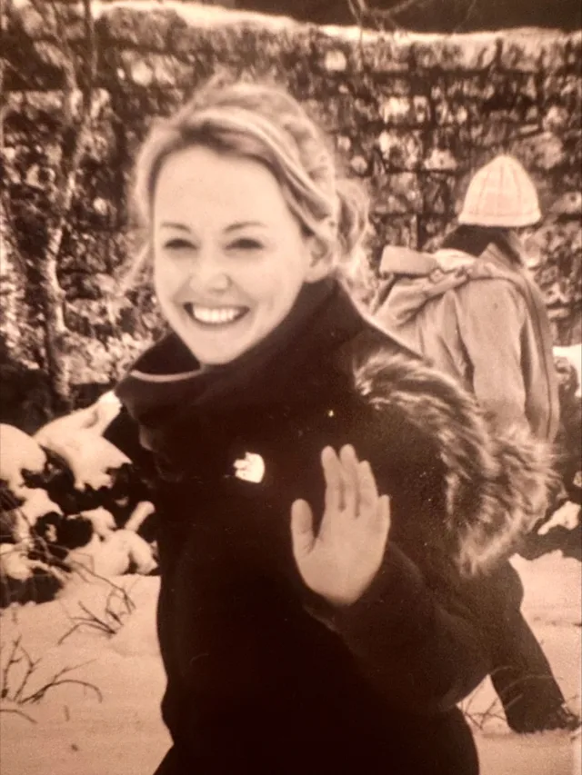 Female student in a black coat smiling and waving at the camera