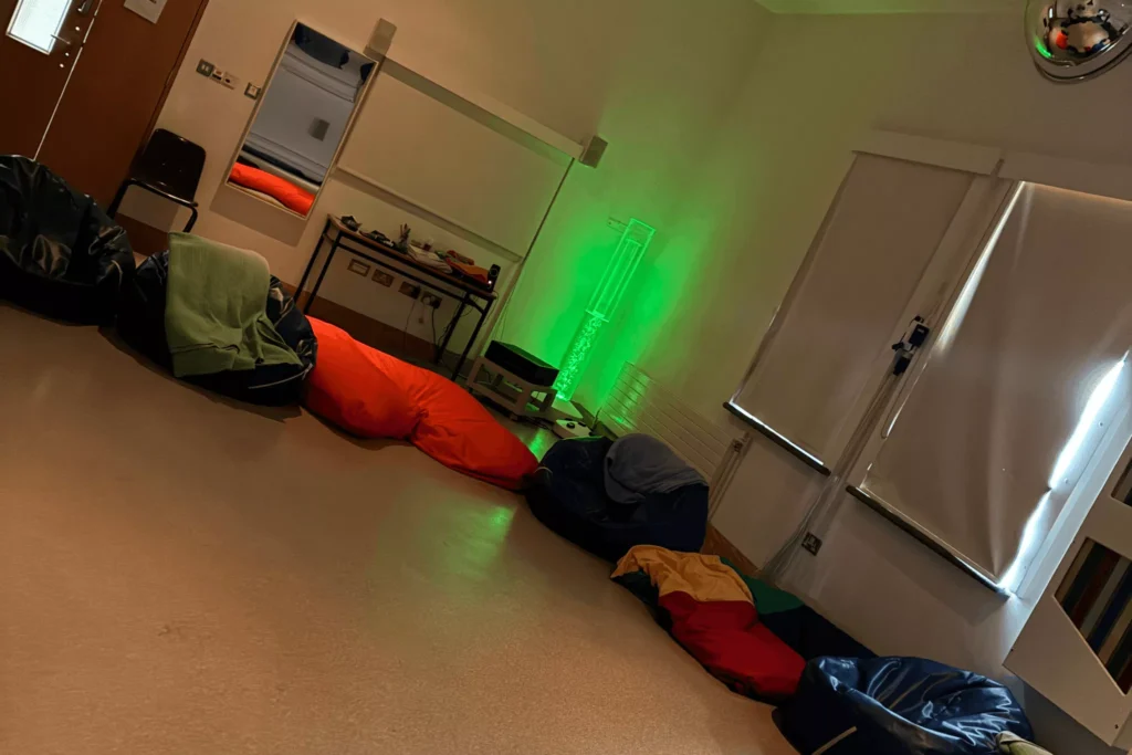 A room with colorful bean bags in various colors (red, green, blue, yellow), with a green light tower in the corner and a mirror reflecting part of the room.