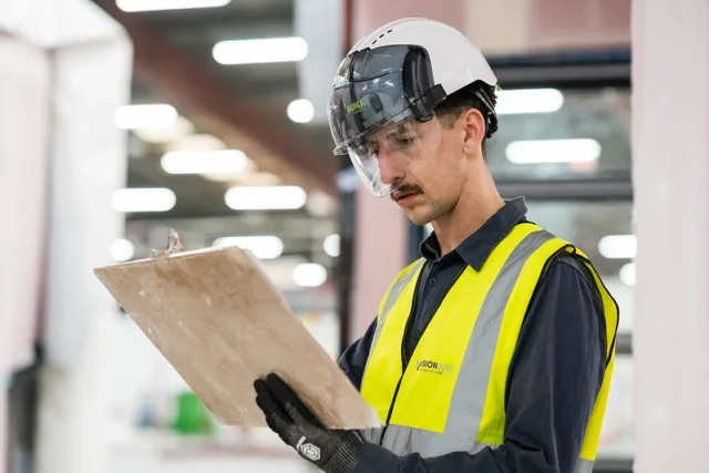 Man in high-ves and helmet looking at clipboard