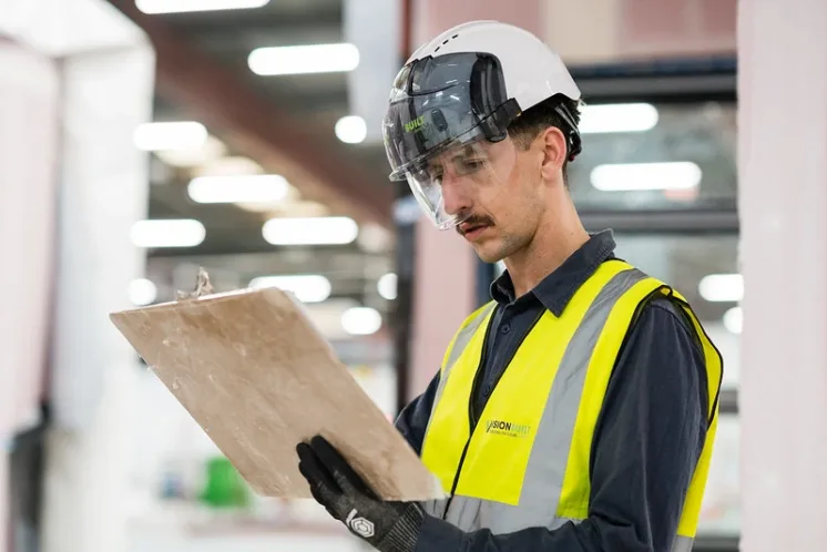 Man in high-ves and helmet looking at clipboard