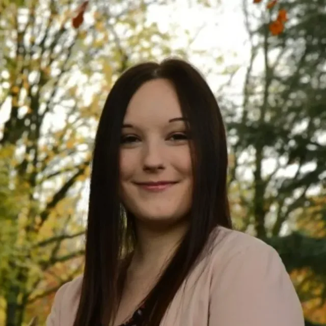 Female Student with long brown hair and wearing a pink jumper