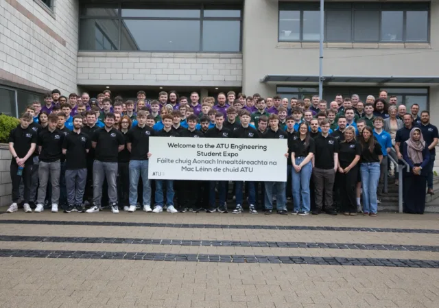 Photograph of a large group of students and faculty standing outside a building, holding a sign that reads "Welcome to the ATU Engineering Student Expo" in English and Irish.
